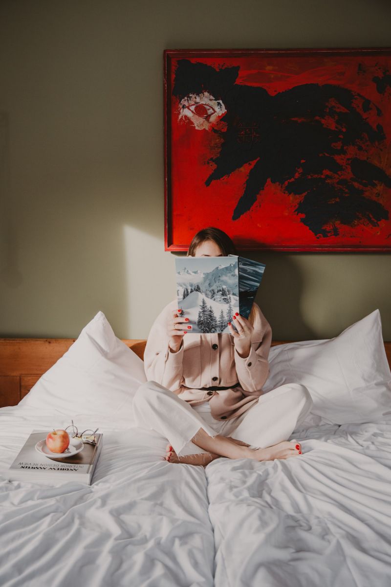 Person reading in bed under contemporary artworks in red | Hotel Seebichl, Kitzbühel, Tyrol – Design Retreat by Lake Schwarzsee, Austria, The Aficionados 
