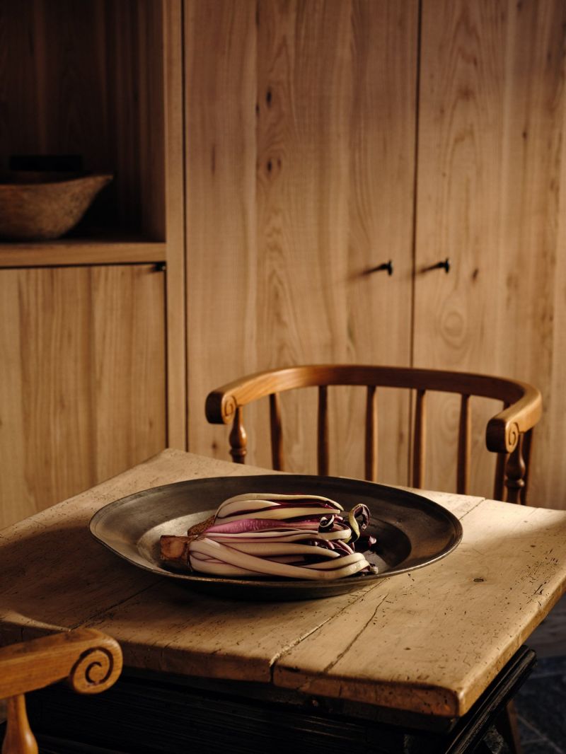 A still life at the Sonnenhof, radicchio on a pewter platter set on a worn stone surface, a spindle-back wooden chair and pale aged timber cupboards behind.