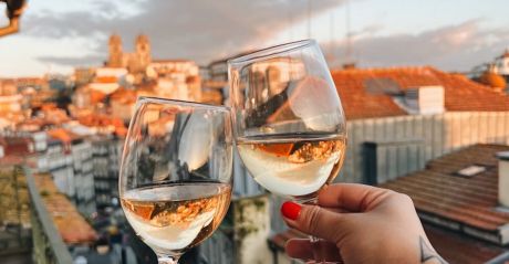 Two hands clinking white wine glasses at golden hour on a B28 Apartments balcony, looking out over Porto's old town to the silhouetted Sé Cathedral | The Aficionados 