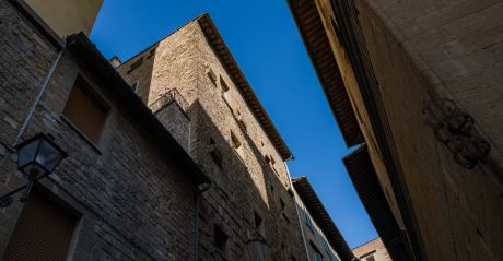 Twelfth-century stone tower-house on Via delle Terme seen from the street, a figure on its corner balcony against a clear blue sky, Terme Historical Tower, images © Tommaso Pini