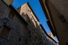 Twelfth-century stone tower-house on Via delle Terme seen from the street, a figure on its corner balcony against a clear blue sky, Terme Historical Tower, images © Tommaso Pini