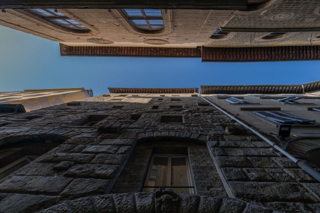 Looking straight up between the rough-stone facades and deep eaves of Via delle Terme, a strip of blue sky between the medieval towers, images © Tommaso Pini