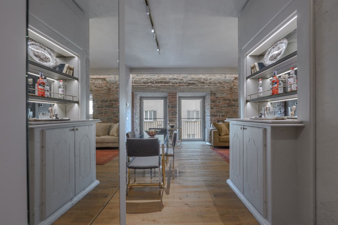 Between mirror-backed bar cabinets to a chrome and brass dining table, bouclé sofas and a wall of exposed stone and brick at Terme Historical Tower, images © Tommaso Pini