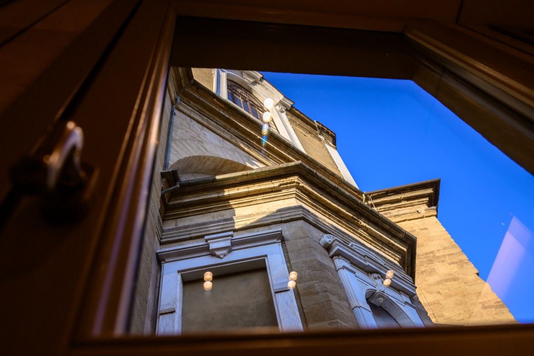 Stone flank of the Medici Chapels framed by an open window at Medici Historical Home, interior lights reflected in the glass, images © Tommaso Pini