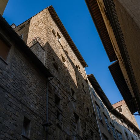 Twelfth-century stone tower-house on Via delle Terme seen from the street, a figure on its corner balcony against a clear blue sky, Terme Historical Tower, images © Tommaso Pini
