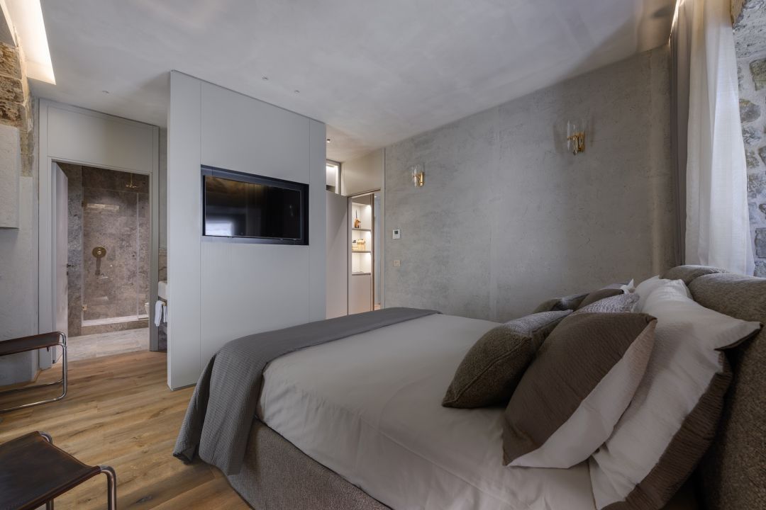 Bedroom in grey plaster with brass wall lights, a chrome-framed leather chair and a travertine shower beyond, Terme Historical Tower, images © Tommaso Pini