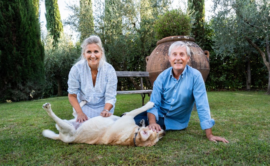 Gianni and Donatella of Florence Luxury Home in a garden of cypresses and olive trees, kneeling on the lawn beside their Labrador,