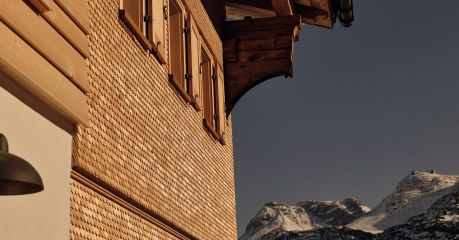 The shingled gable of Haus W in Zug at dusk, timber shutters below deep carved eaves, snow peaks beyond.