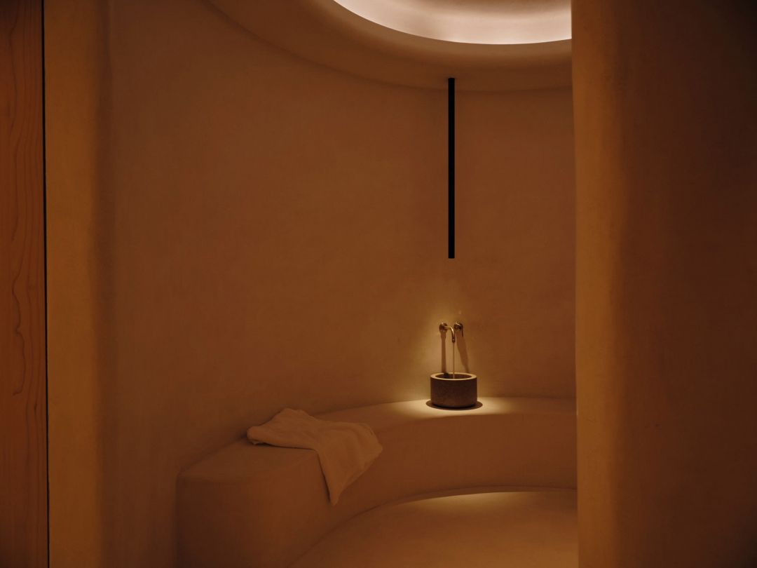 The spa at Haus W, curved walls in soaped lime turning without a hard edge, a small stone basin and light hidden in the cove above the bench.