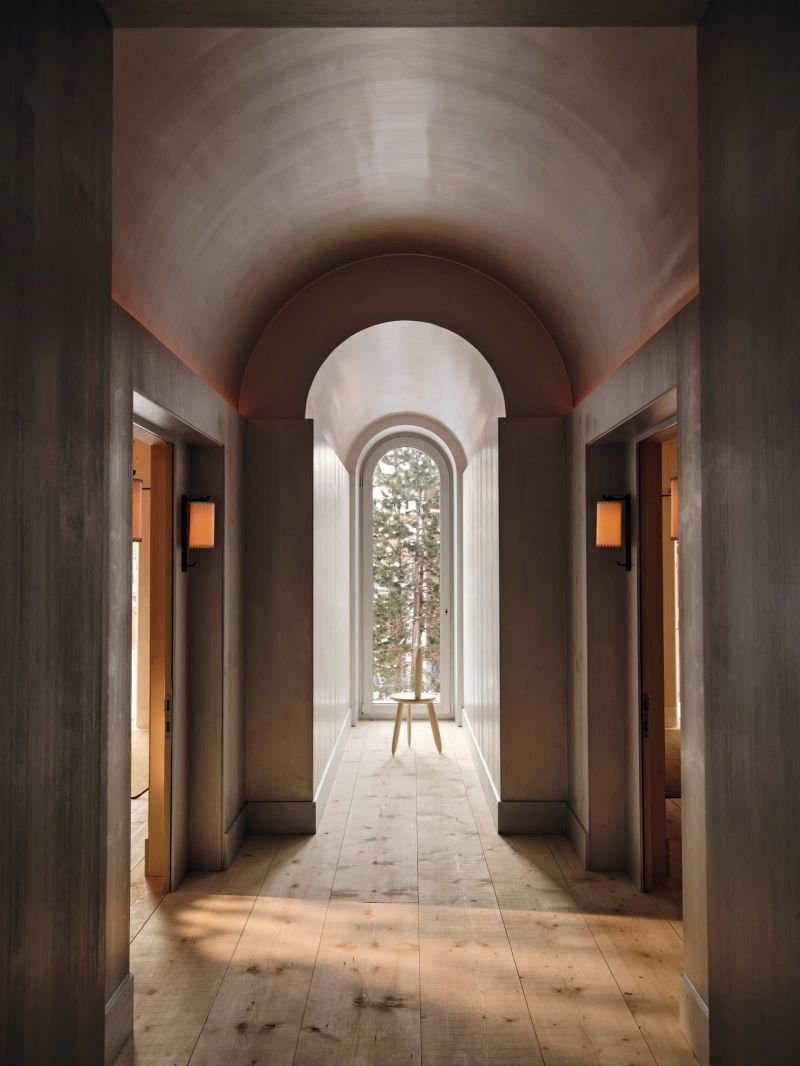 The barrel-vaulted bedroom corridor at Haus W, soft grey walls curving to an arched window with a tripod stool by Aldo Bakker beneath it.