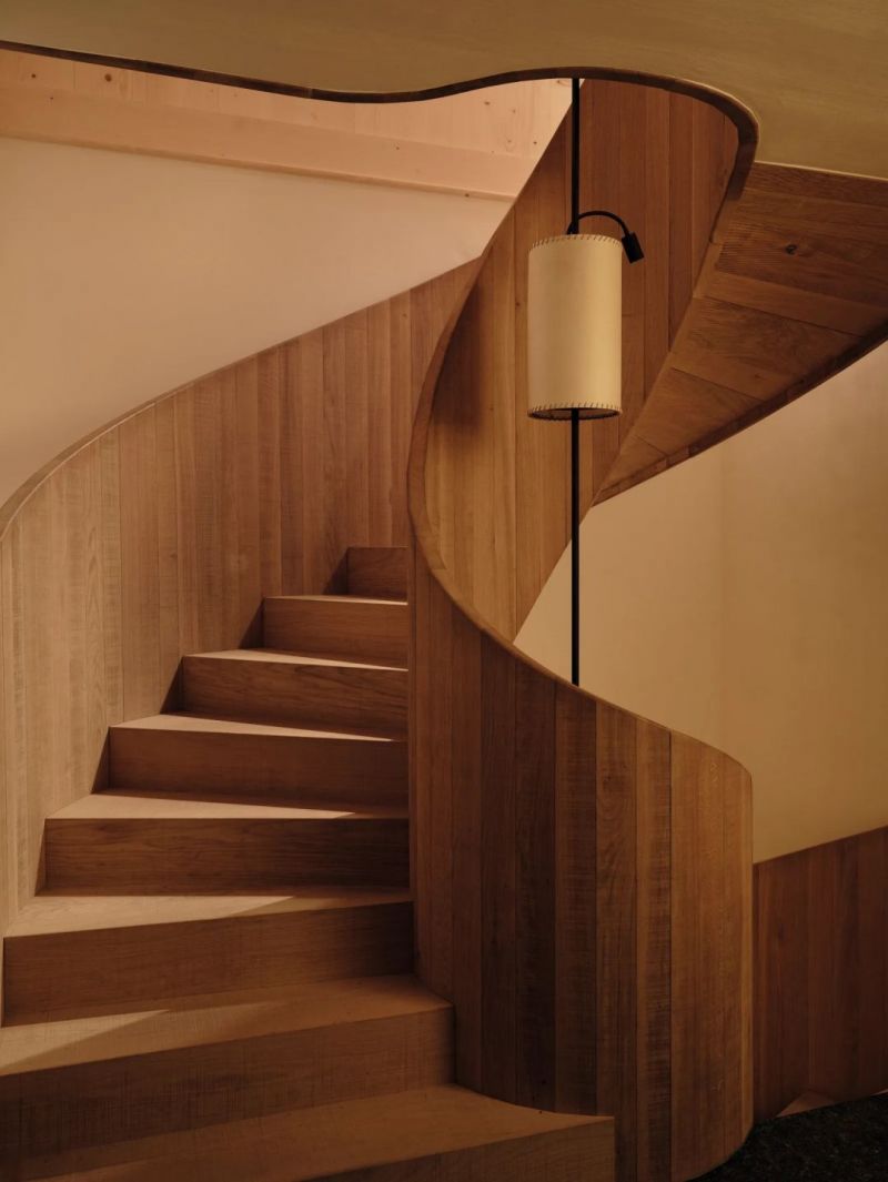 The oak spiral staircase at Haus W, its balustrade carried in one curved surface, a parchment shaded lamp hanging in the well.