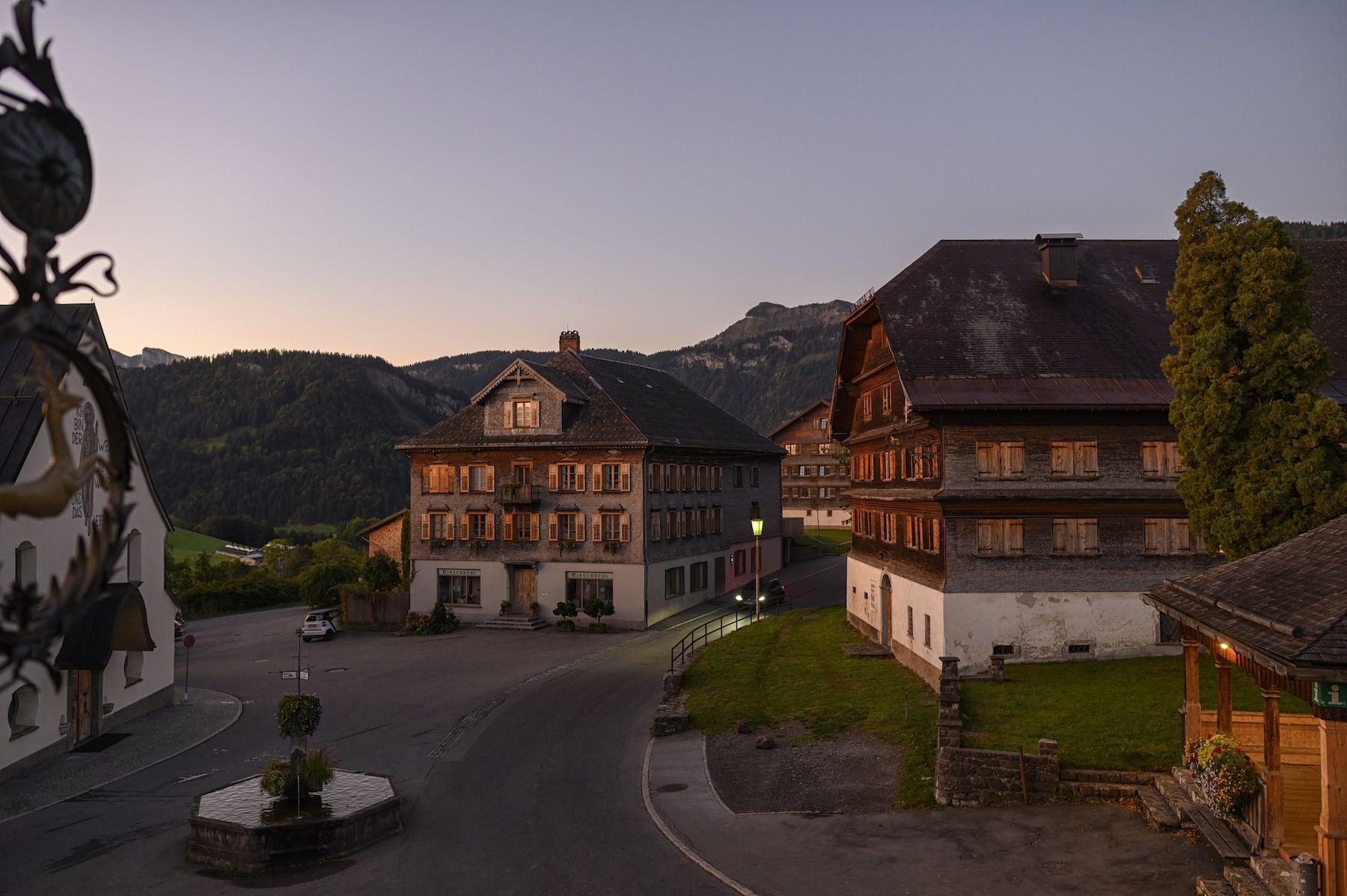 The Hirschen at dusk on the village square in Schwarzenberg, Bregenzerwald, its lit timber façade below the Vorarlberg peaks.