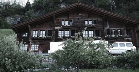 Classic timber chaltet of Bernese Overland: Haus Mannenberg at dusk, seen through a laden apple tree in the foreground, shuttered windows and steep chalet roofline behind,