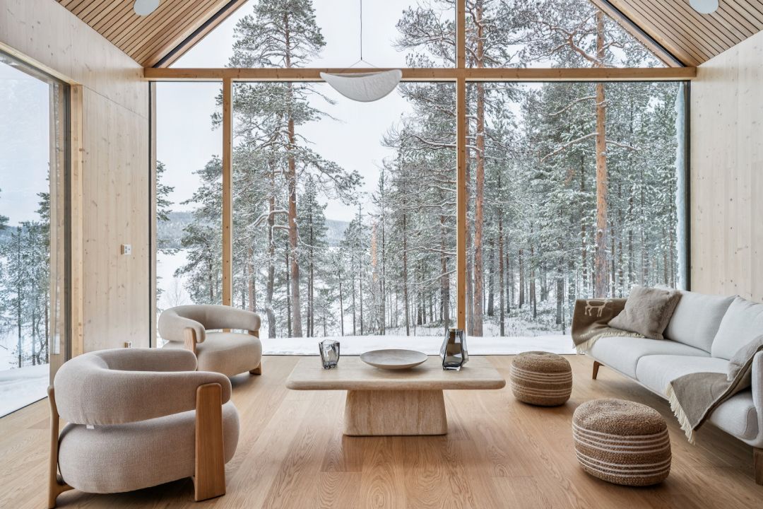 Lounge interior by Kati Anglé and Tapani Takkunen with contemporary Nordic furnishings and panoramic windows framing Lake Inari: Inai Haven Lapland: Luxury Private-Hire Contemporary Timber Villas on Lake Inari, Finland.