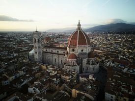 Aerial view of Florence at dusk, Brunelleschi’s terracotta dome crowning the cathedral of Santa Maria del Fiore beside Giotto’s campanile, the city’s roofs stretching to the Tuscan hills.