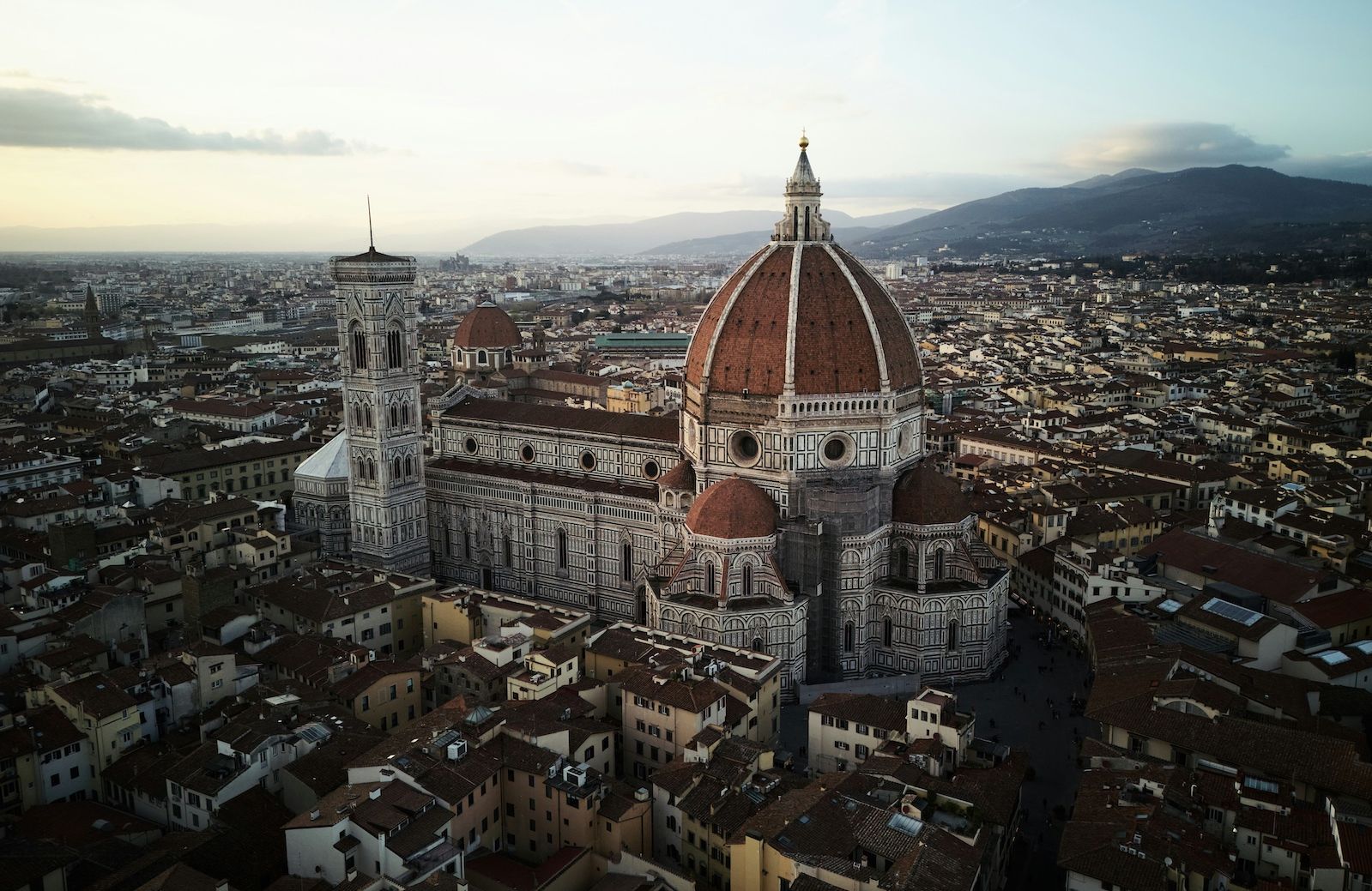 Aerial view of Florence at dusk, Brunelleschi’s terracotta dome crowning the cathedral of Santa Maria del Fiore beside Giotto’s campanile, the city’s roofs stretching to the Tuscan hills.
