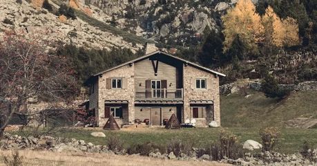 The stone and timber exterior of L'Ovella Negra in the Vall d'Incles, Andorra, with the open-sided pavilion, festoon lights and hay bales on the grass. Caption: The lodge and its pavilion at the head of the valley, hay bales still on the grass.