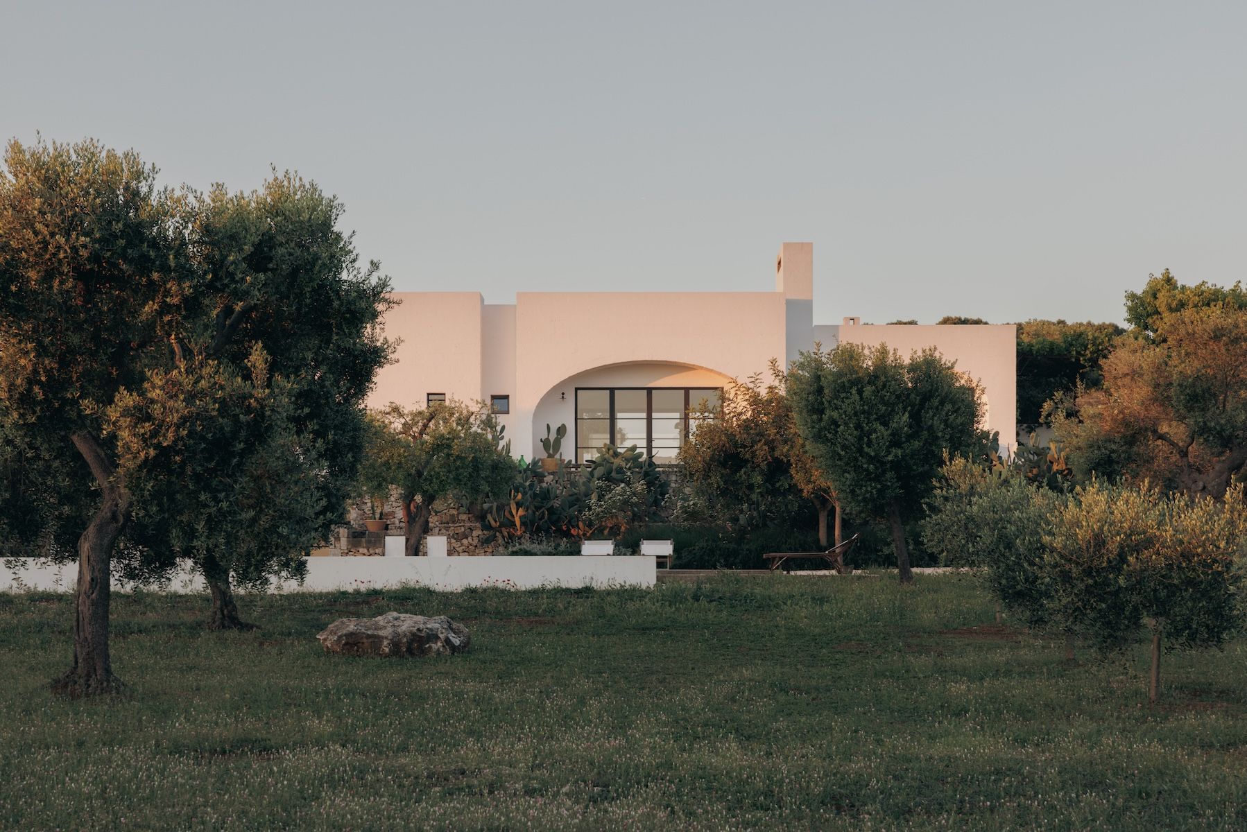 S/un Set over the rural guesthouse-hotel Masseria Moroseta caught pink in the dusk light, its arched Crittall window framed by olive trees and prickly pear, near Ostuni, Puglia | The Aficionados.
