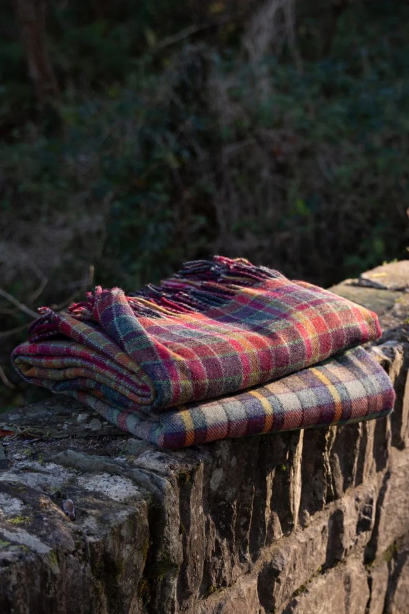 Person sitting looking at the Pembrokshire coast wrapped in a blanket | Melin Tregwynt | Artisan Blankets Woven in Wales - A British Hertiage Brand | TheAficionados.com