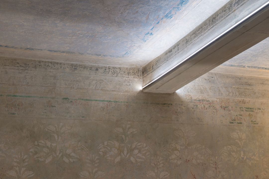 Faded fresco recovered during restoration at Santa Croce Historical Home, a stencilled frieze of foliage and green bands on the wall, traces of blue on the ceiling above.