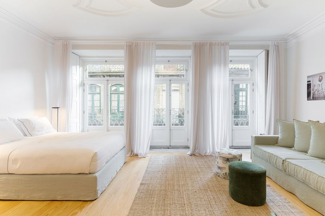 Principal-floor bedroom at B28 Apartments Porto with elaborate 19th-century stucco ceiling and three tall French doors opening to wrought-iron balconies.| The Aficionados 