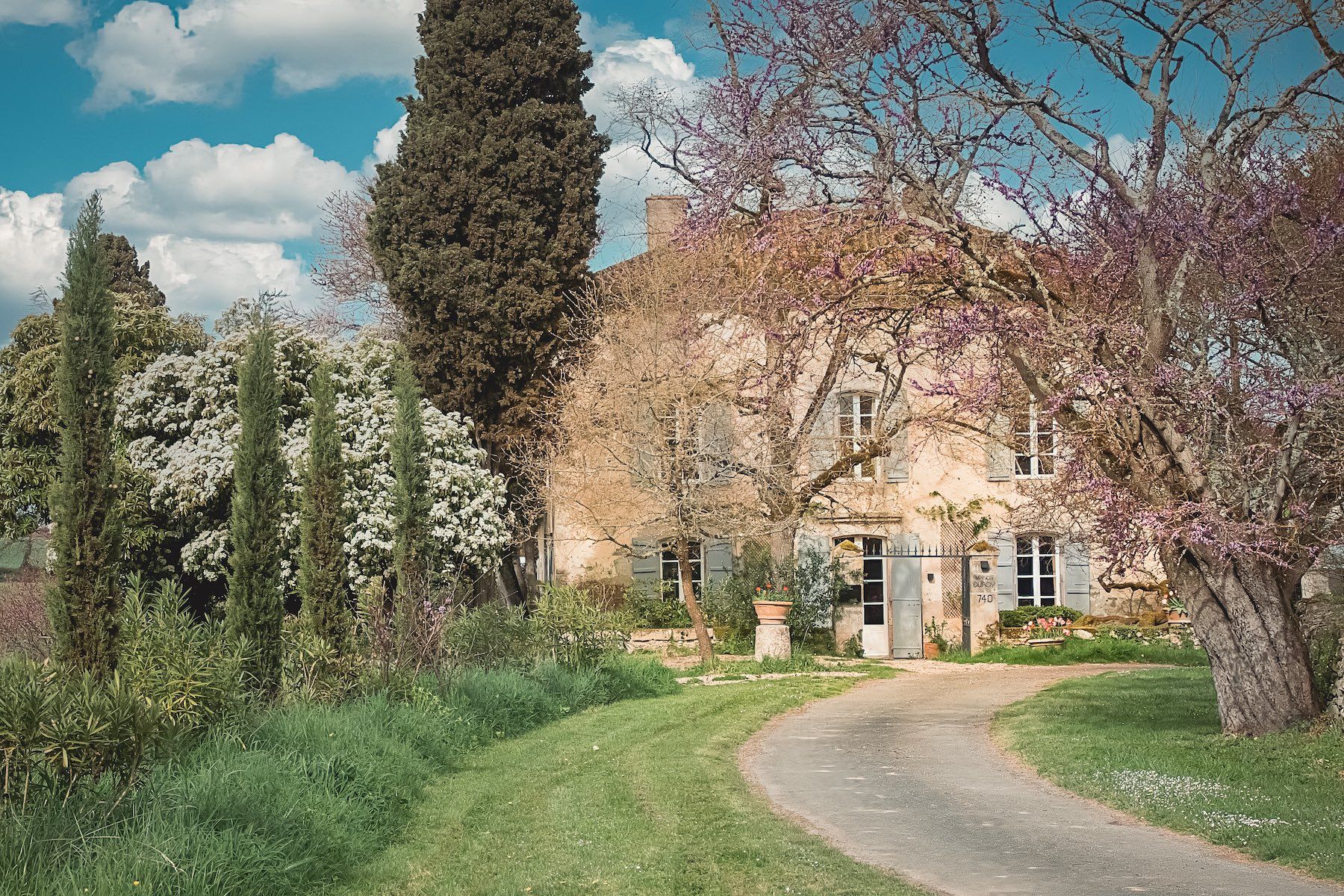 Maison Duroy exterior spring view pink Judas tree blooms honeyed stone facade vert de gris shutters Gascogne countryside | The Aficionados