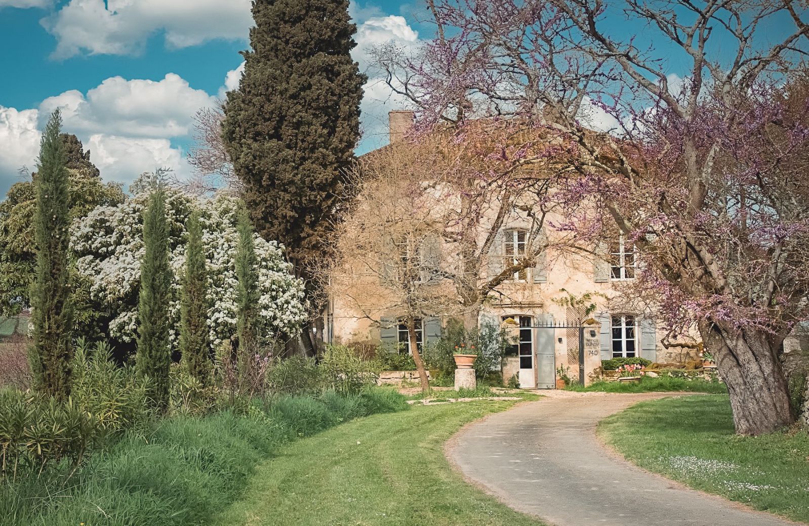 Maison Duroy exterior spring view pink Judas tree blooms honeyed stone facade vert de gris shutters Gascogne countryside | The Aficionados