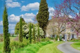 Maison Duroy exterior spring view pink Judas tree blooms honeyed stone facade vert de gris shutters Gascogne countryside | The Aficionados