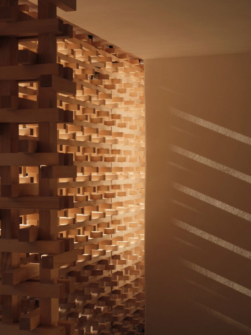 Detail of Shinichiro Ogata's interlocking spruce block screen at Haus W, daylight striping the plaster wall beside it.