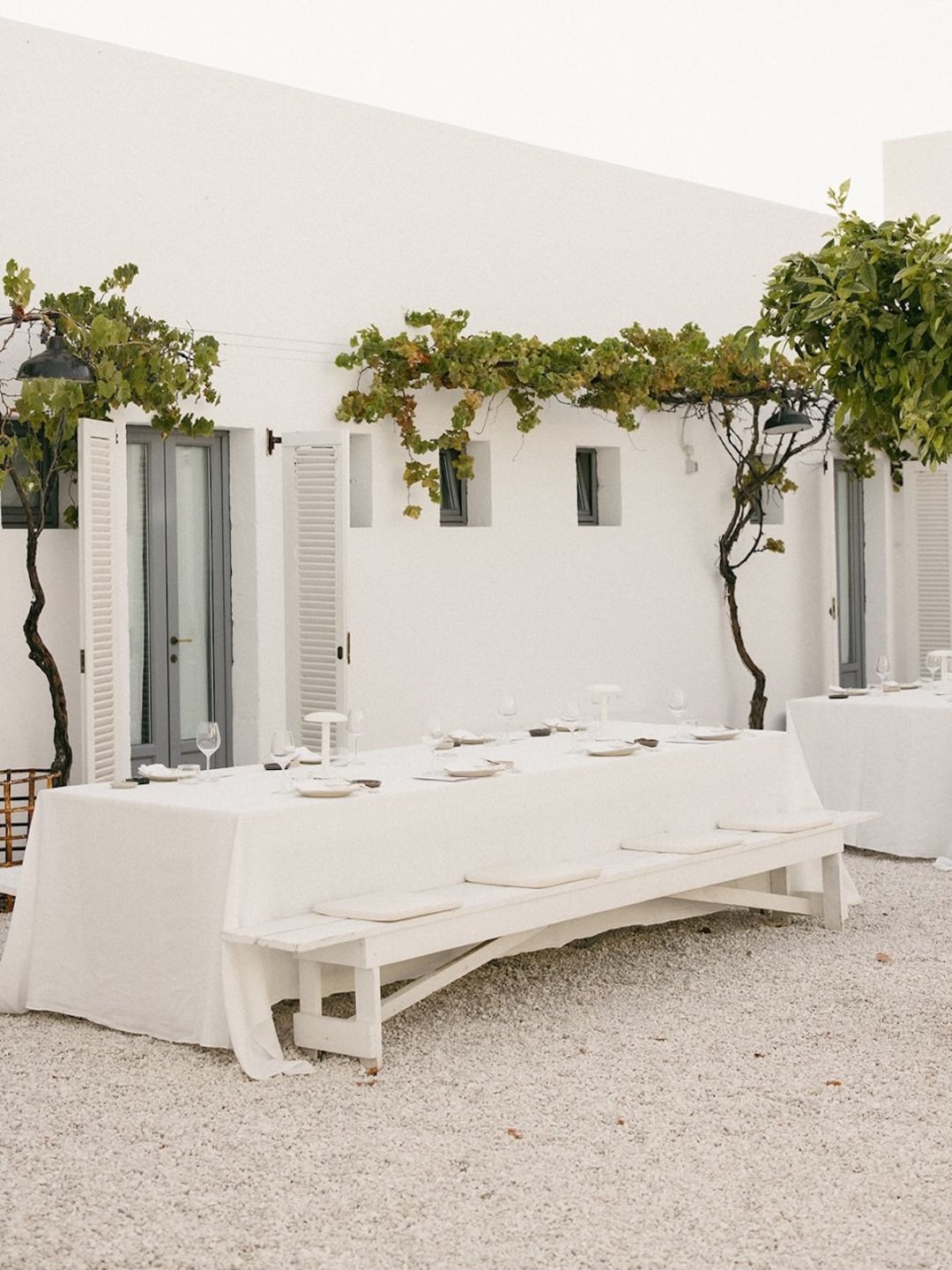 The communal long table laid for dinner beneath a grapevine pergola, dove-grey shutters behind, Masseria Moroseta, Ostuni, Puglia | The Aficionados.