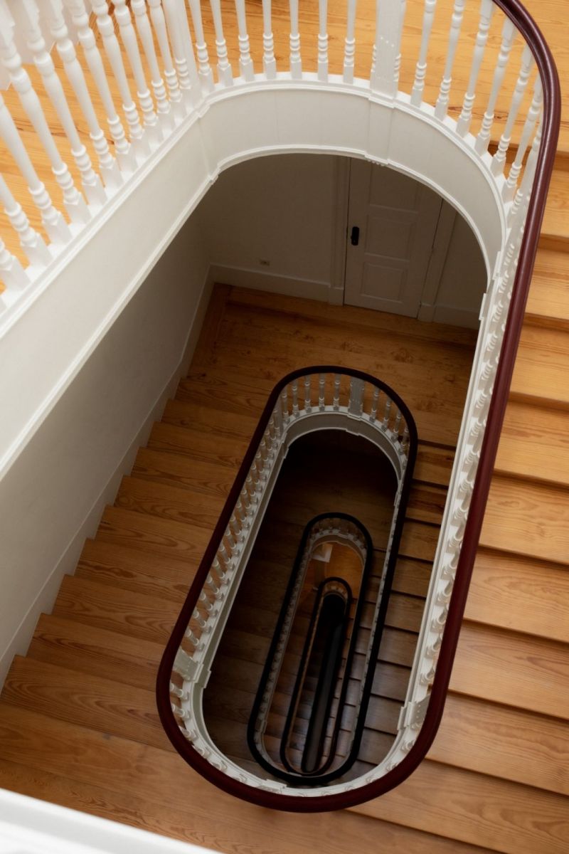The restored 19th-century spiral staircase at B28 Apartments Porto, looking down through five floors with turned white balusters and a mahogany handrail. | The Aficionados 