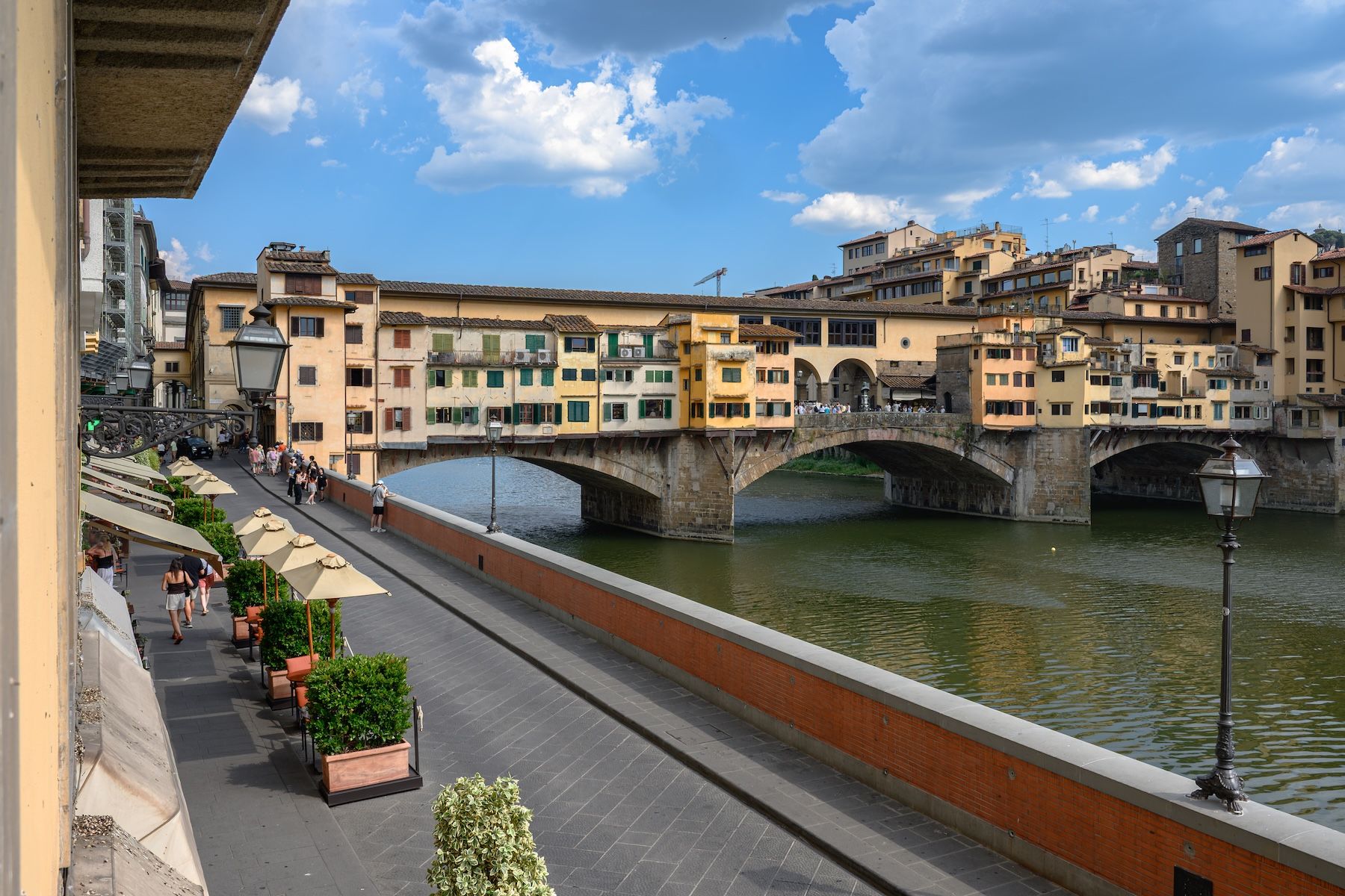Ponte Vecchio seen from a first-floor balcony on Lungarno Acciaiuoli, its overhanging shops above the Arno and café umbrellas below, images © Tommaso Pini