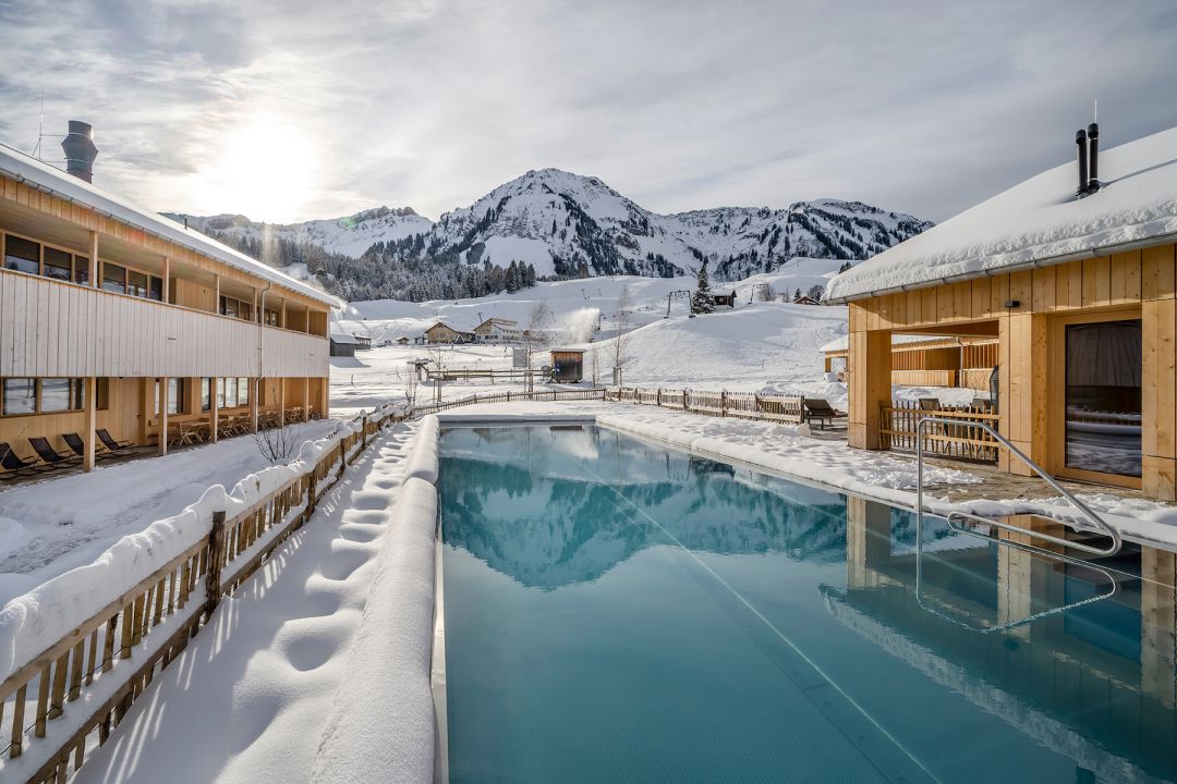 Winter image swimming outdoor heated pool int he Alps / mountain backdrop with snow blue pool | Fuchsegg Eco Lodge, Bregenzerwald – Design Hotel in the Austrian Alps, Vorarlberg