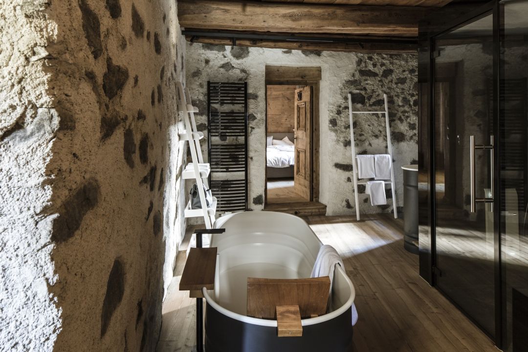 Standalone Bathtub in balck metal with white interior Desginer Pieces against heritage stone walls of the Weisses Kreuz Hotel | Agape: Sculptural Bathroom Design Across Iconic Hotels | The Aficionados 