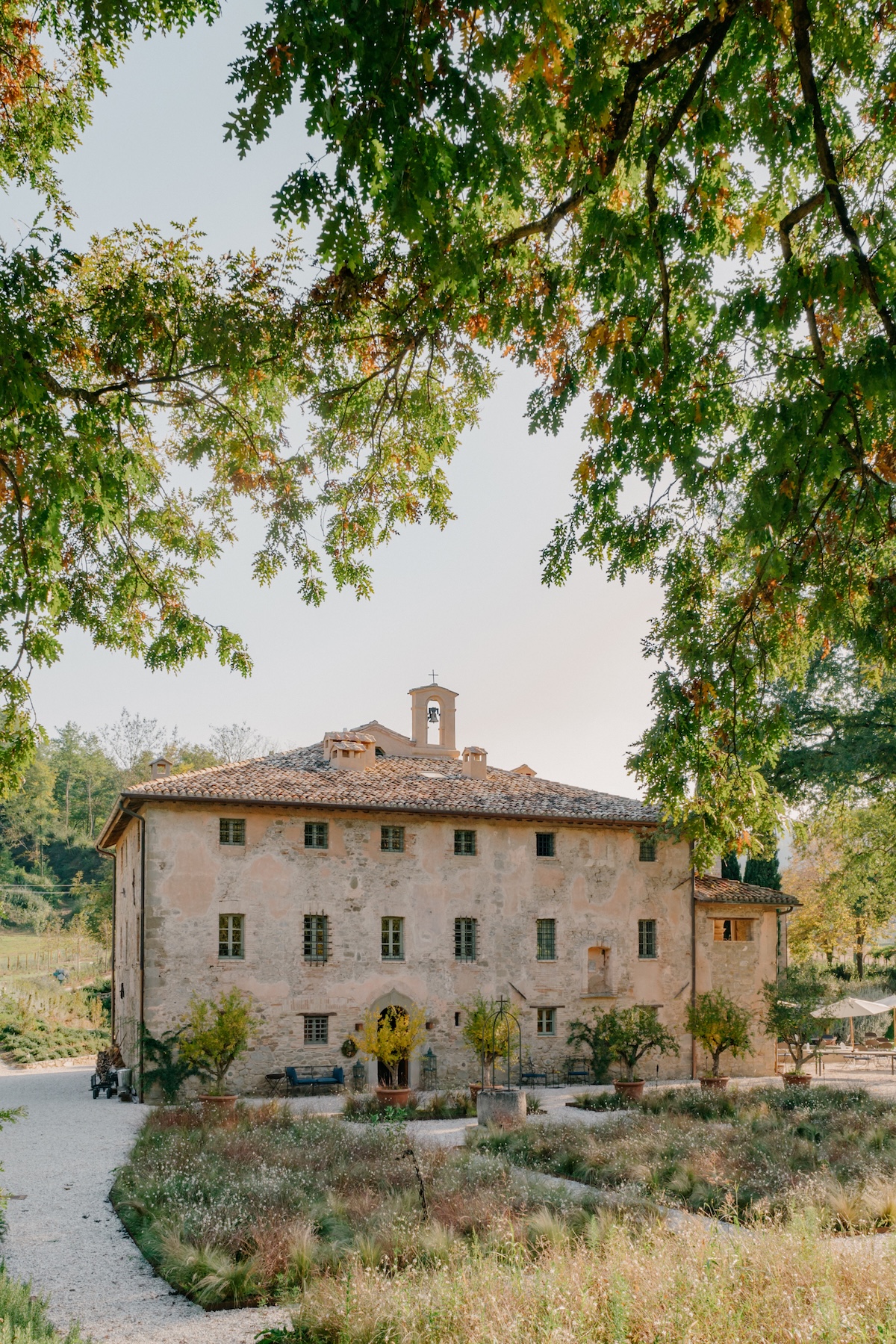 A restored stone convent in the Italian countryside framed by oak branches above a gravel garden, a Rustico design hotel | The Aficionados