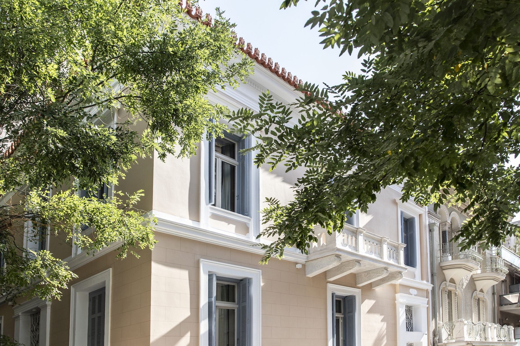 The peach-plaster neoclassical façade of Monsieur Didot, a six-suite design guesthouse-hotel in the Kolonaki quarter of Athens, framed by street trees.