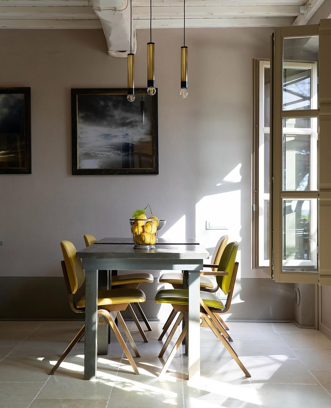 Sunlit boutique dining room with yellow leather chairs, a bowl of lemons and moody framed seascapes