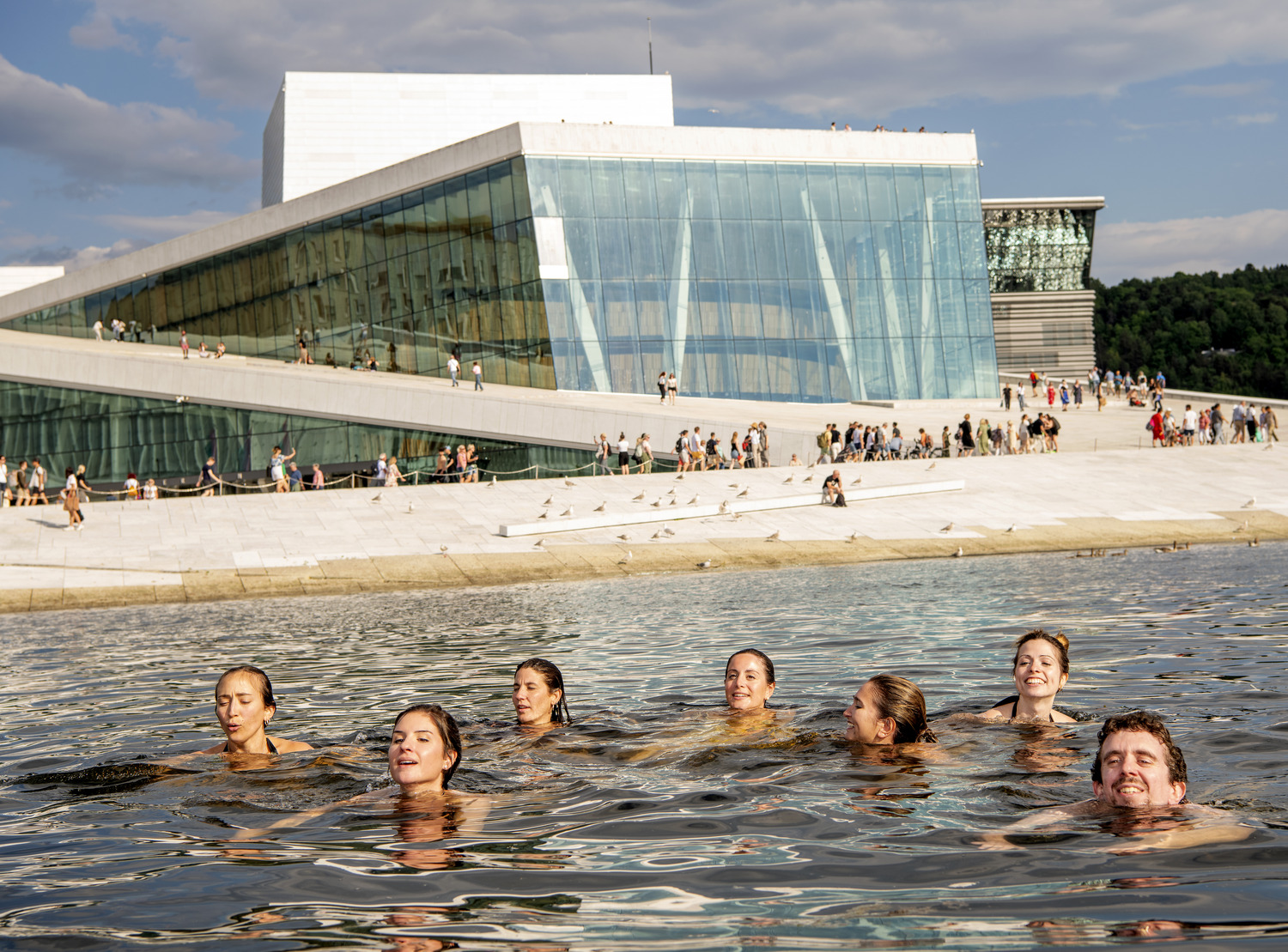 Swimmers in the Oslofjord in front of Snøhetta’s Oslo Opera House, visitors strolling up its sloping white stone roof | The Aficionados