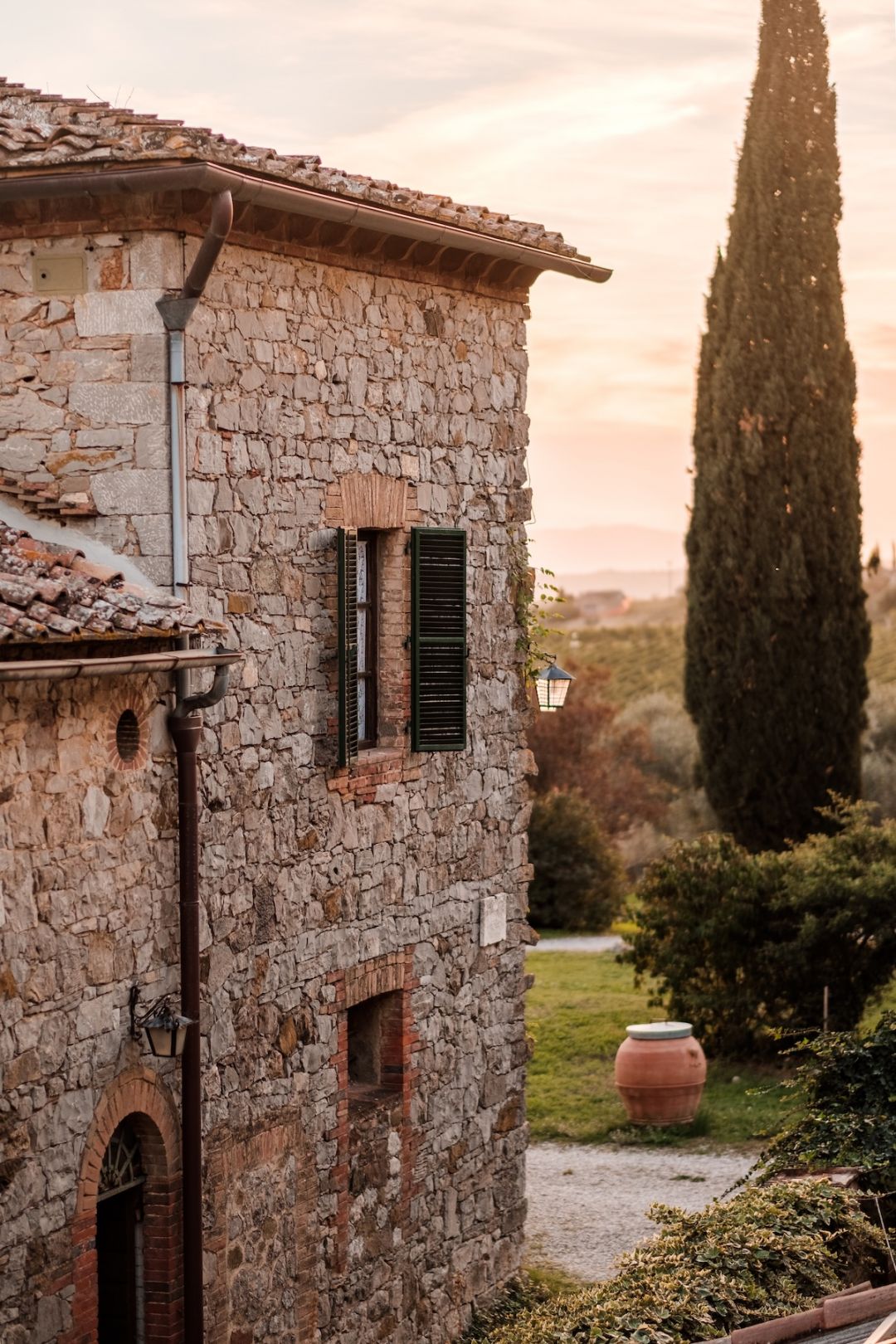 Restored 1720 stone farmhouse courtyard at Colle ai Lecci borgo in Chianti Classico, with terracotta paving and olive-green shutters | The Aficionados