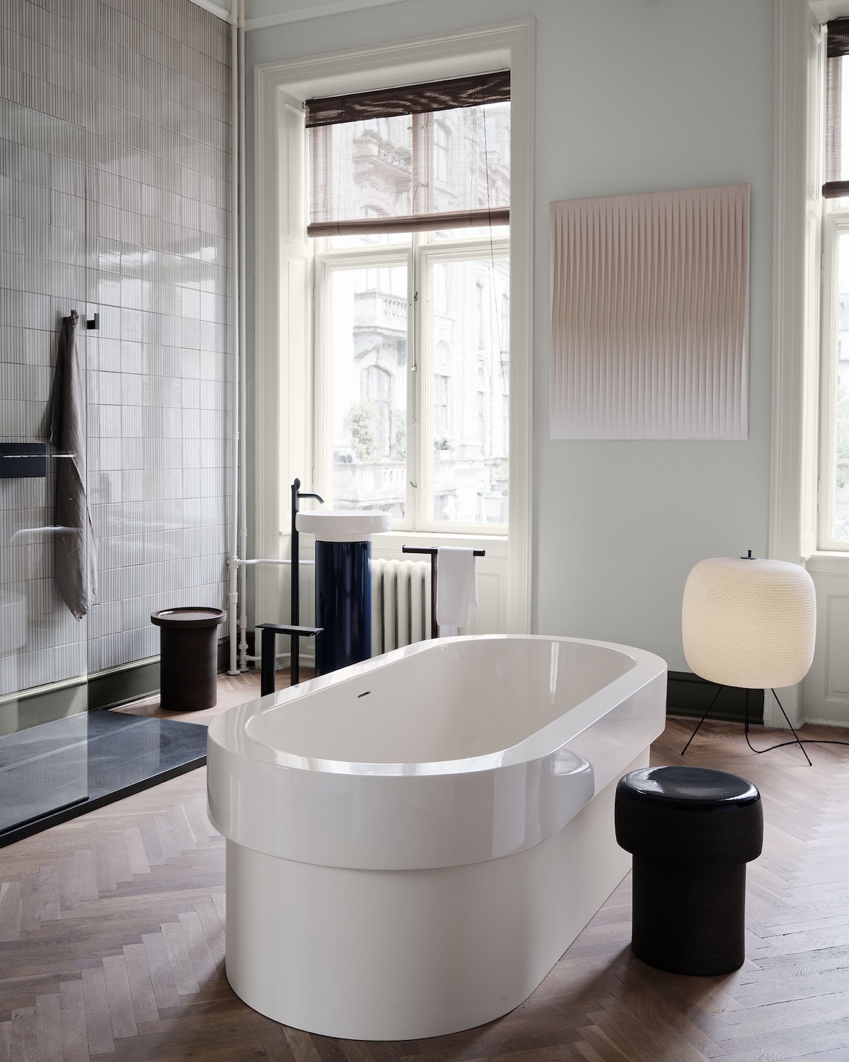 Agape bathroom at 3daysofdesign: white freestanding Cenote bathtub on herringbone parquet, with a blue gloss pedestal washbasin, black floor-mounted tap and a woven paper floor lamp.