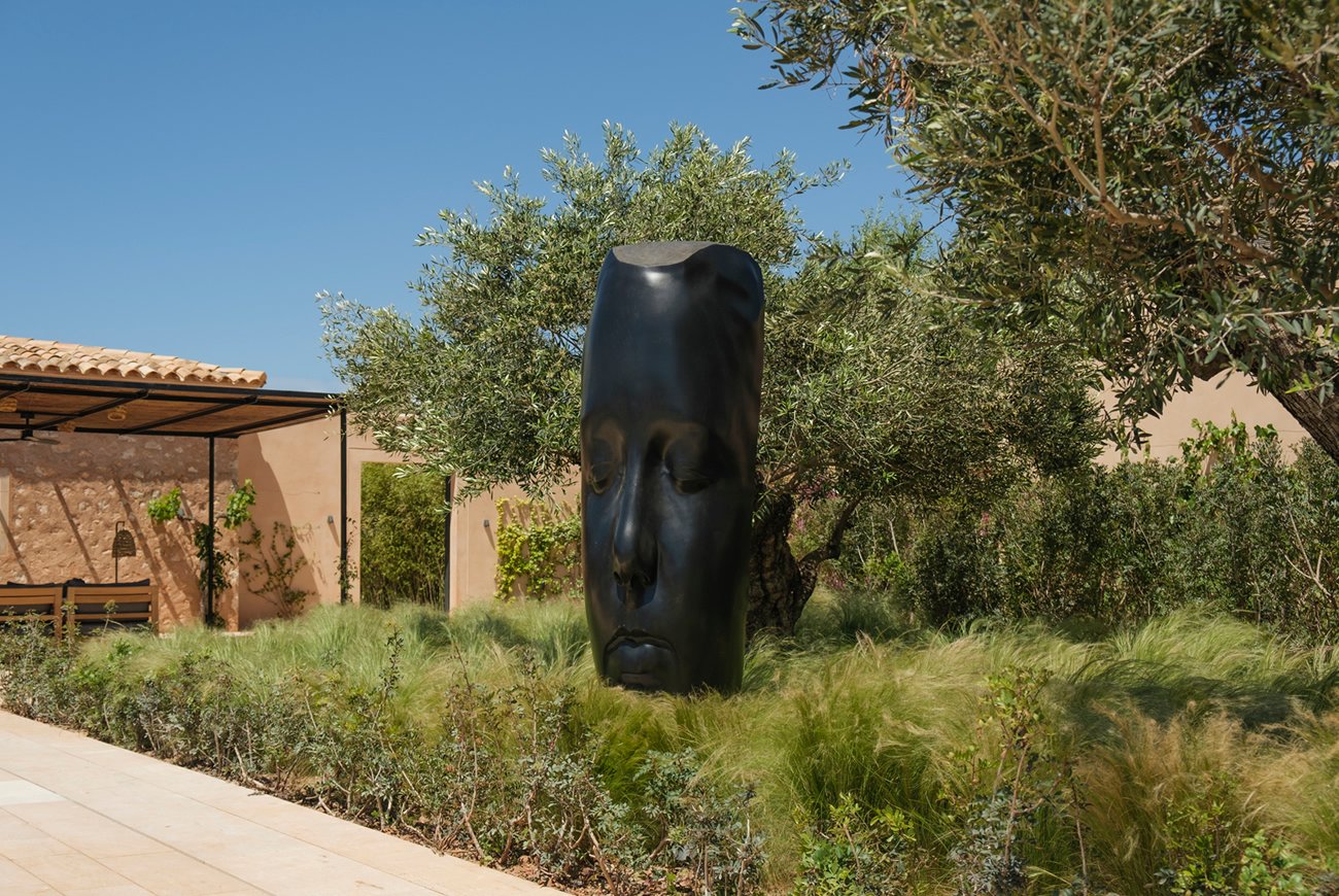 Jaume Plensa's dark bronze head among olive trees and grasses in the garden at Can Ferrereta, Santanyí | The Aficionados