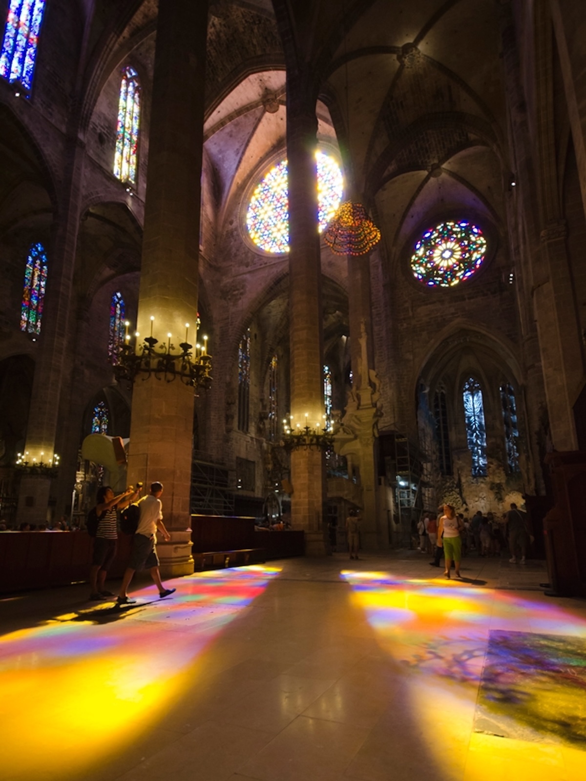 Coloured light from the stained glass of La Seu pooling across the stone floor as visitors walk through it | The Aficionados