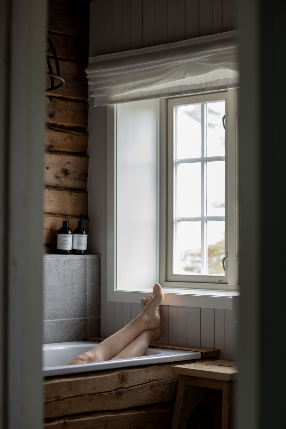 A quiet bath by a window in a timber rorbu at Nusfjord Resort & Village, Lofoten, with amenity bottles on the sill | The Aficionados