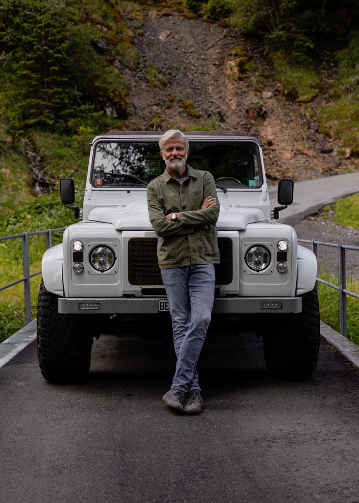 Grant Maunder stadngin in front of white Defender Land Rover in the Alps | Owner of hotel The Brecon in Adelboden | Manmade: 12 Hotels Shaped by Men of Design and Style