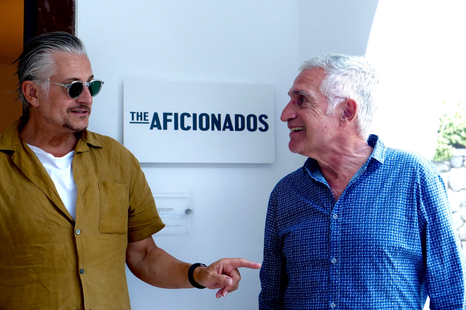 Iain Ainsworth, Giorgos, George Alexiou | Two handsome guys talking in front of a hotel plaque from The Aficionados |Family Ties & Design Minds – Hotels, Style & Flavour Shaped by Kinship