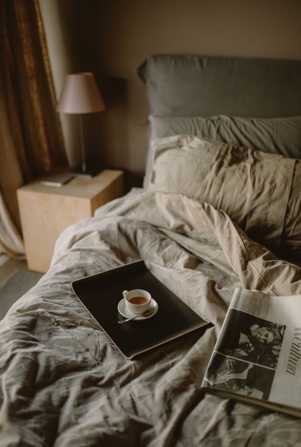 VIVERE SUITES ARCO | Espresso and a magazine on a tray across rumpled linen sheets in a moody boutique hotel bedroom