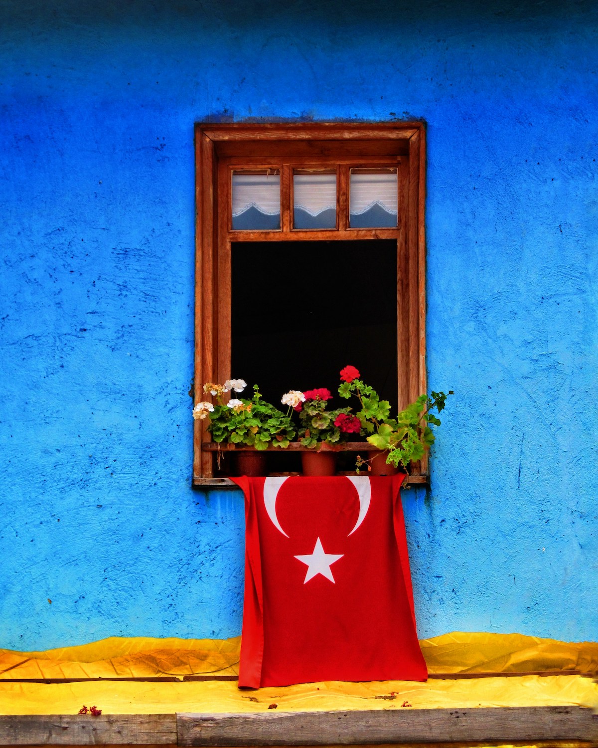 Flag of Türkiye in red hanging against a blue wall and yellow paving vivid surround of a traditional village house window |Untamed Beauty of Türkiye’s Riviera: A Journey Through Ancient Bays and Forested Shores