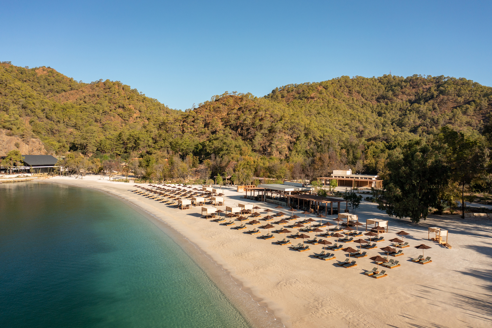 Pristine Beach Cove with a few sun loungers luxury beach against hills and trees, blue sky |Günlüklü Bay: Türkiye’s Hidden Forested Cove of Natural Luxury