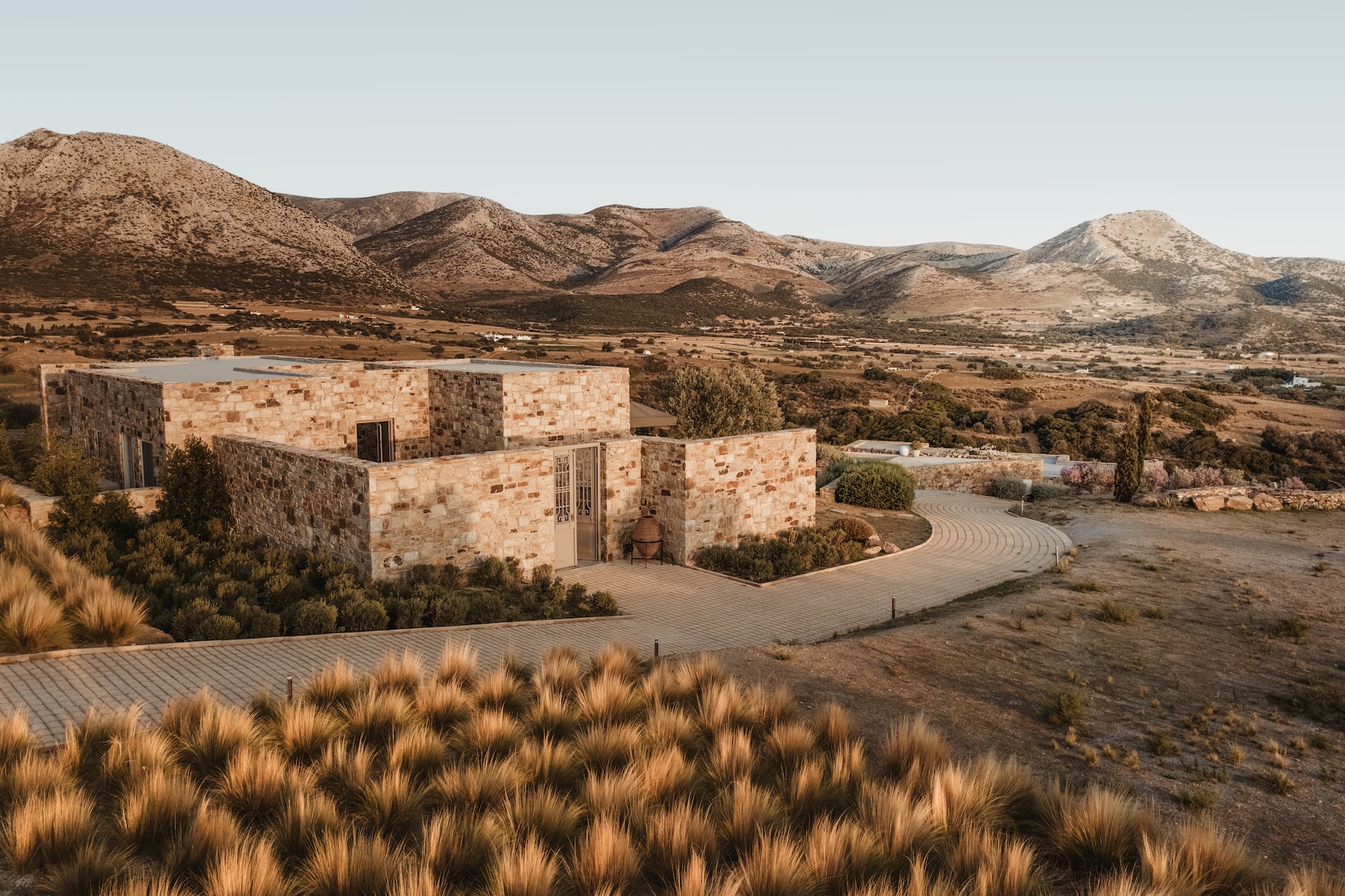 The honeyed Sangri-stone volumes of Ayiopetra on Naxos, Greece, standing on ancestral land against dry mountains at golden hour.