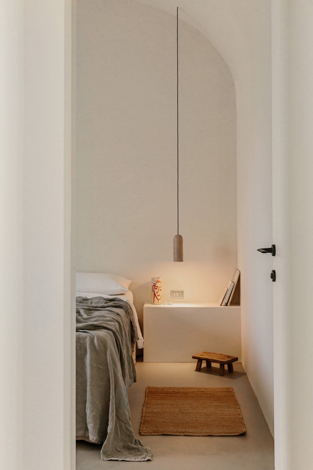 A minimalist whitewashed bedroom with an arched alcove, linen bedding and a jute rug, in the Contemporary register | The Aficionados